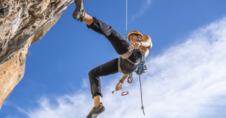 A woman rockclimbing wearing a helmet and using ropes 