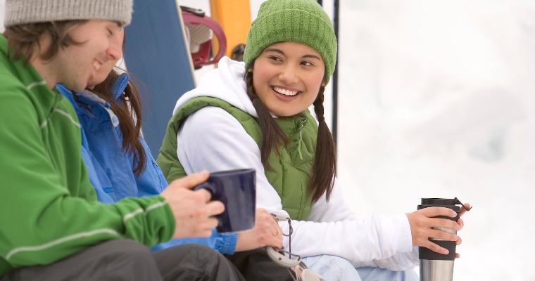 Three people sitting down, drinking from thermos' on a ski field