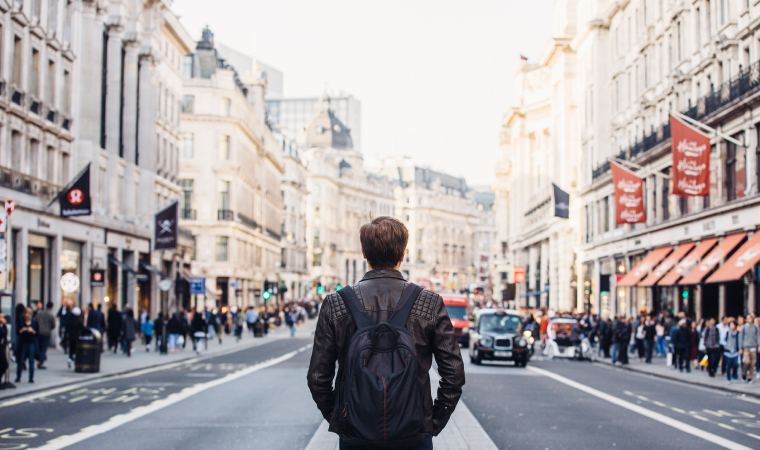 A man walking in the middle of a street in London, wearing a backpack
