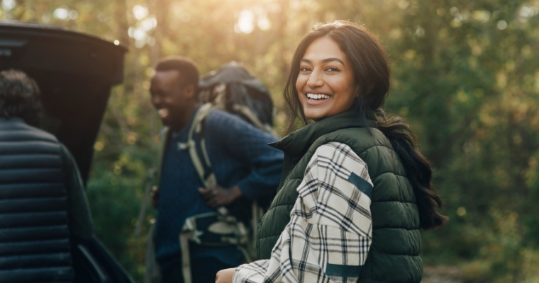 A woman on a hiking trip smiling, with people wearing hiking clothes and backpacks around her.