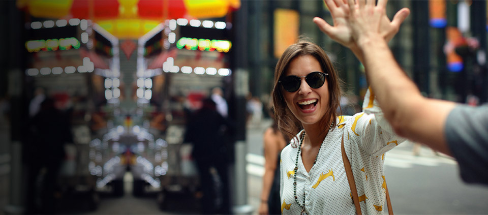A woman in a white and yellow shirt wearing sunglasses, high fives a person on a busy city street